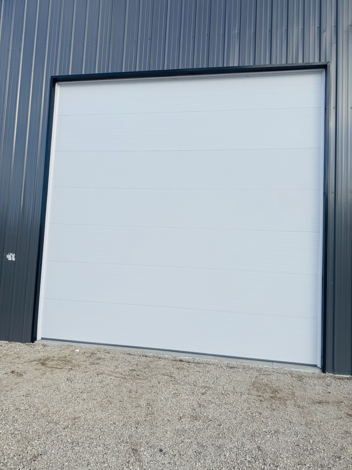 Large white commercial sectional garage door installed on a metal pole barn building
